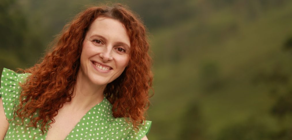 Woman with red hair, wearing green polka dot dress smiling