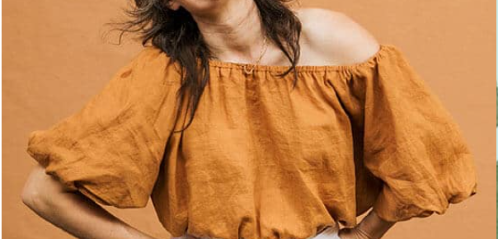 Ange Nennie - Woman wearing a brown top and white pants with hands inside the pockets, smiling