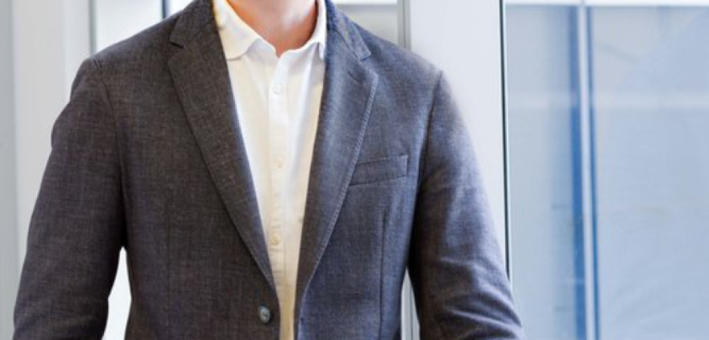 Man in a business casual attire standing up near a window, smiling