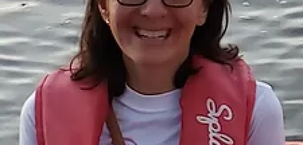 Woman in a lake wearing white shirt, glasses and a life vest smiling