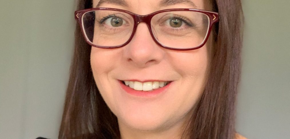 Photo of Rebecca Reid. Woman with brown hair wearing glasses smiling